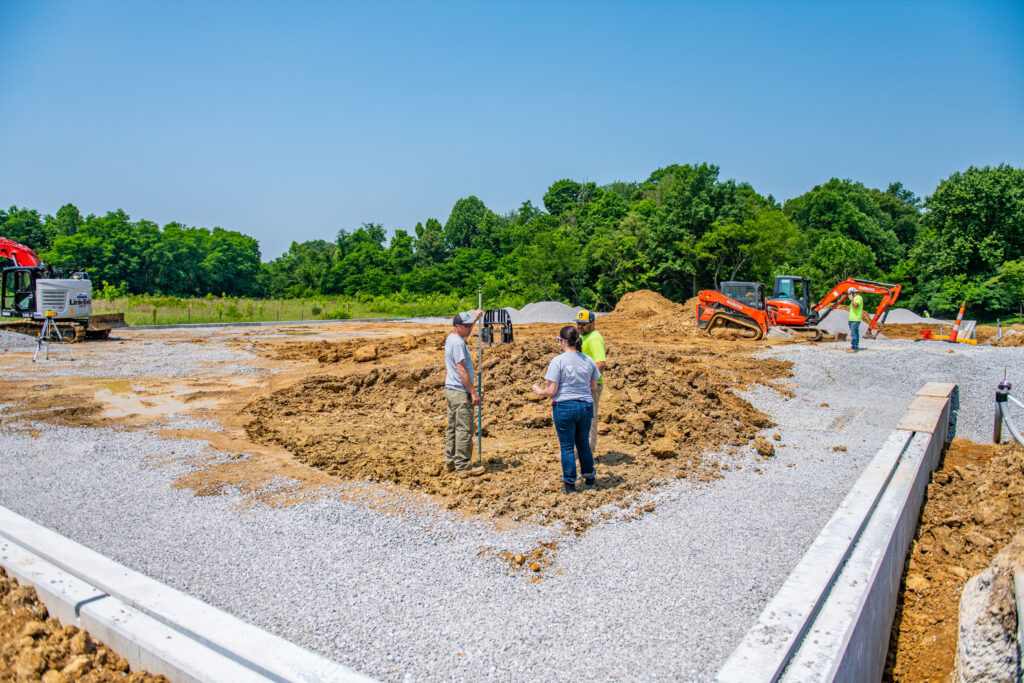 Commercial construction crew and project managers reviewing layout and site planning on an active gravel-ground renovation site in Indiana and Kentucky.